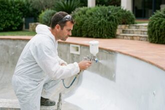 Technicien appliquant du gel-coat sur la paroi intérieure d'une piscine résidentielle vide en extérieur